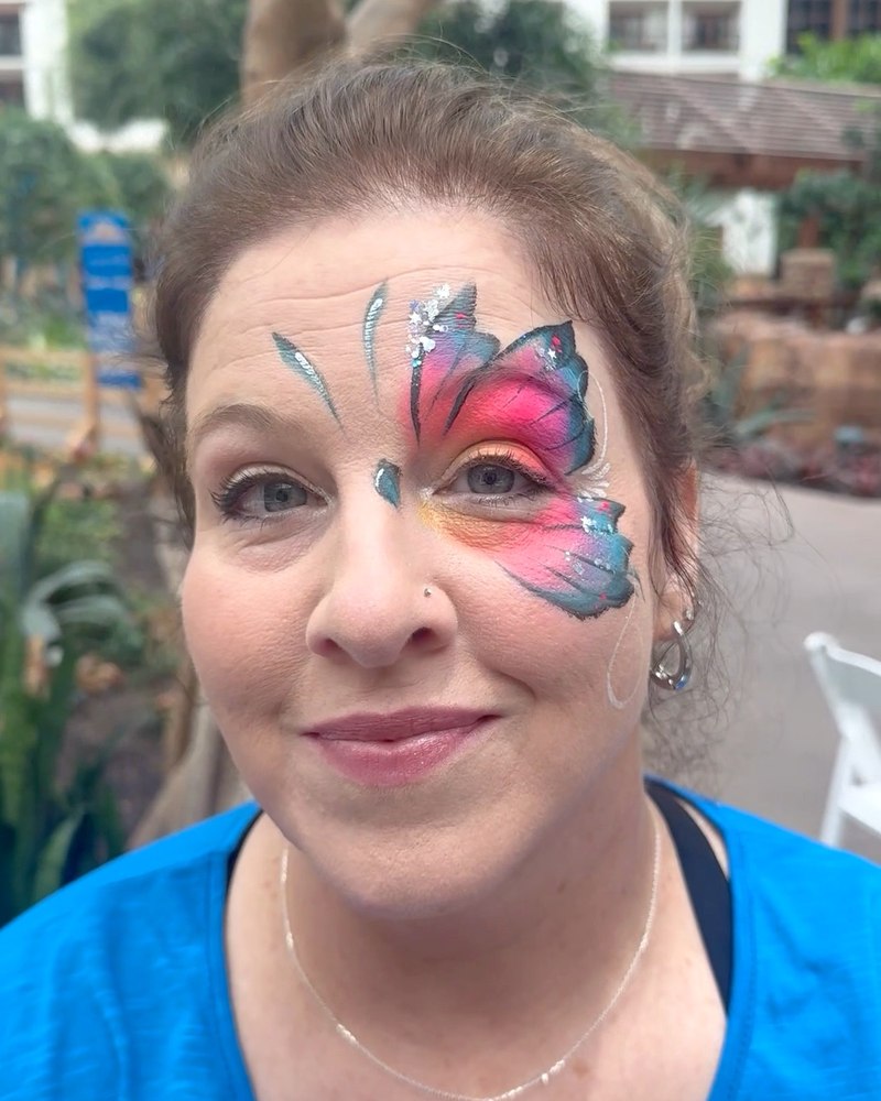 Adult guest wearing colorful butterfly face painting by CandyProArt